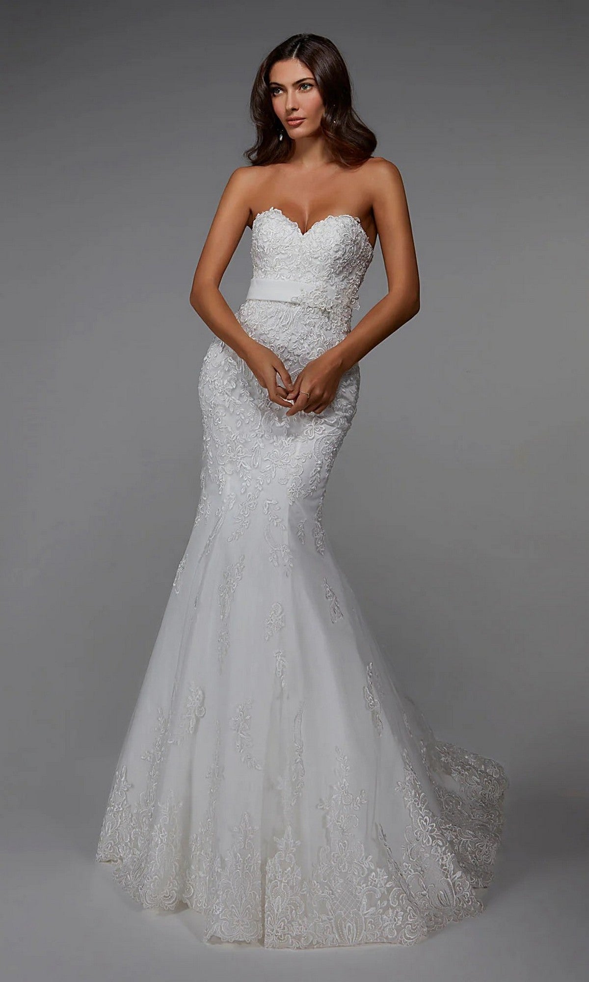 A woman models the Alyce 7032 long white dress in ivory, a strapless bridal gown with a sweetheart neckline, lace embroidery, and a mermaid tulle skirt, posing against a plain gray background.